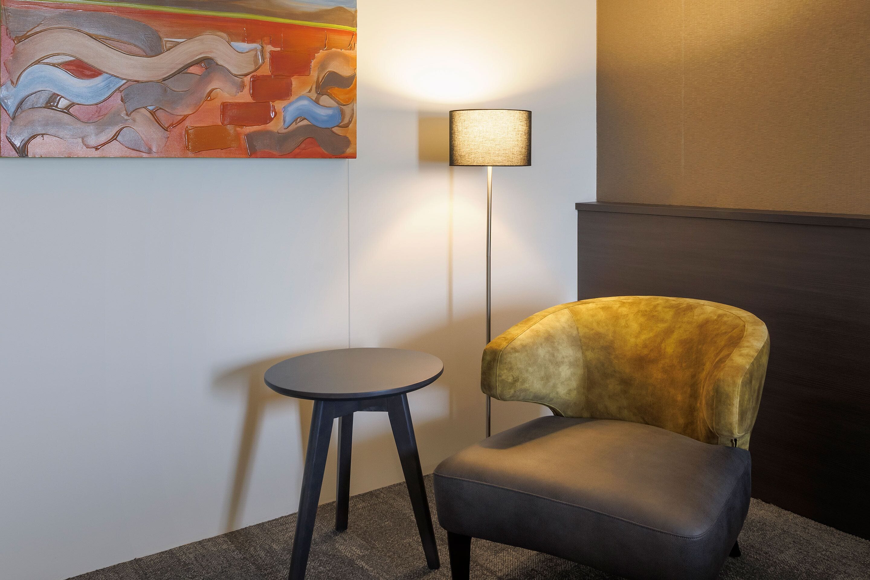 Une pièce avec un fauteuil moderne, une petite table ronde et un lampadaire.
