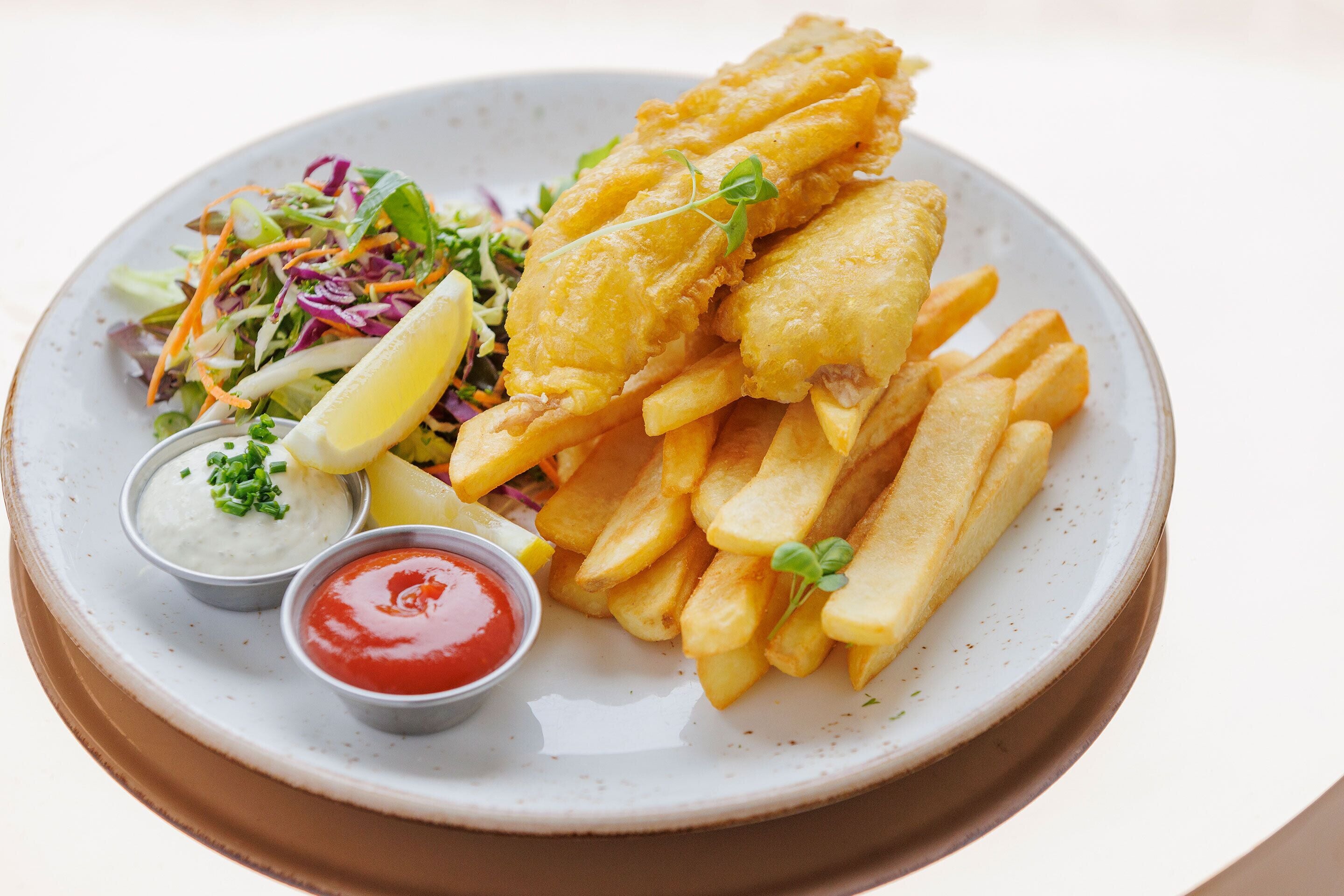 Une assiette de poisson-frites accompagnée d’une salade et de deux sauces pour tremper.