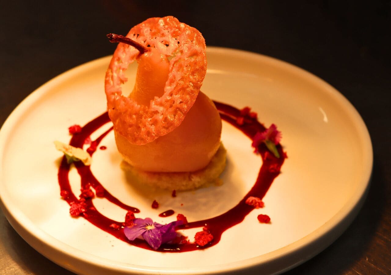 A dessert on a white plate with a decorative element on top and a red sauce design.