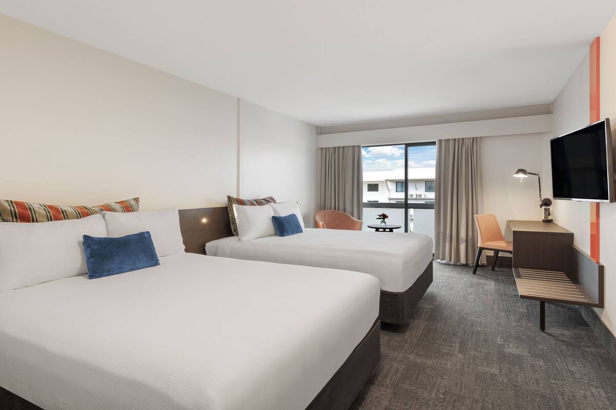 A hotel room with two beds, a desk, a chair, a TV, and a window with curtains.