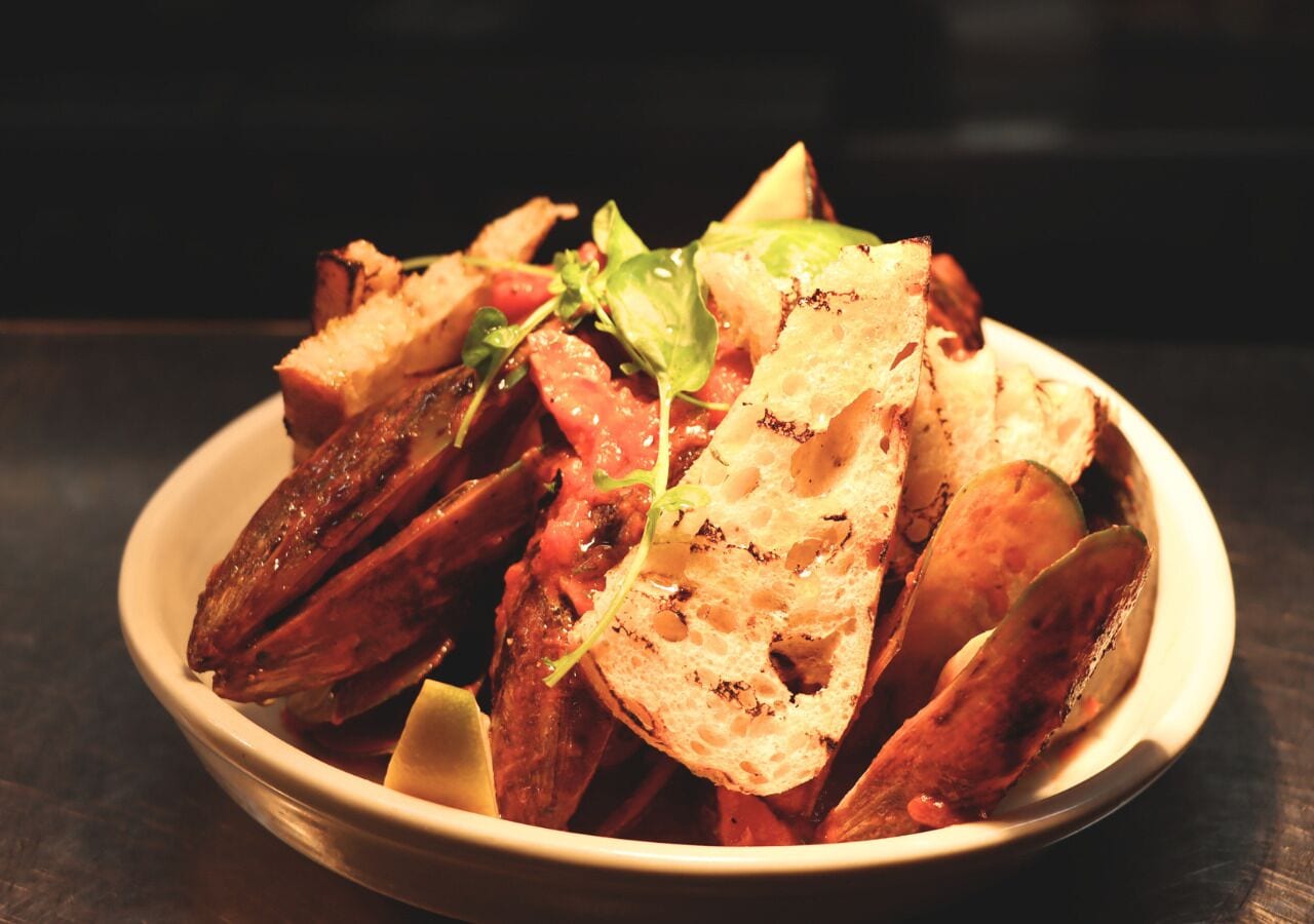A bowl of roasted potatoes with slices of bread and a garnish of greens.