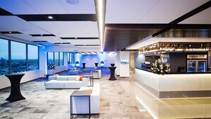 A modern hotel lobby with a bar area, seating arrangements, and large windows offering a city view.