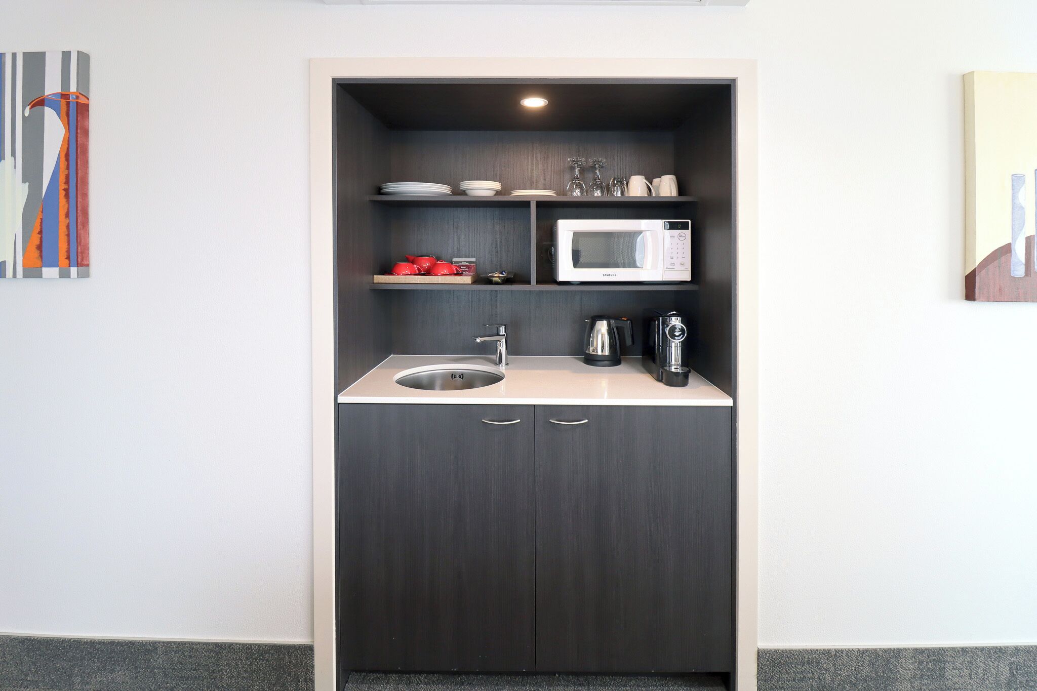 A compact kitchenette with a microwave, coffee maker, and a sink.