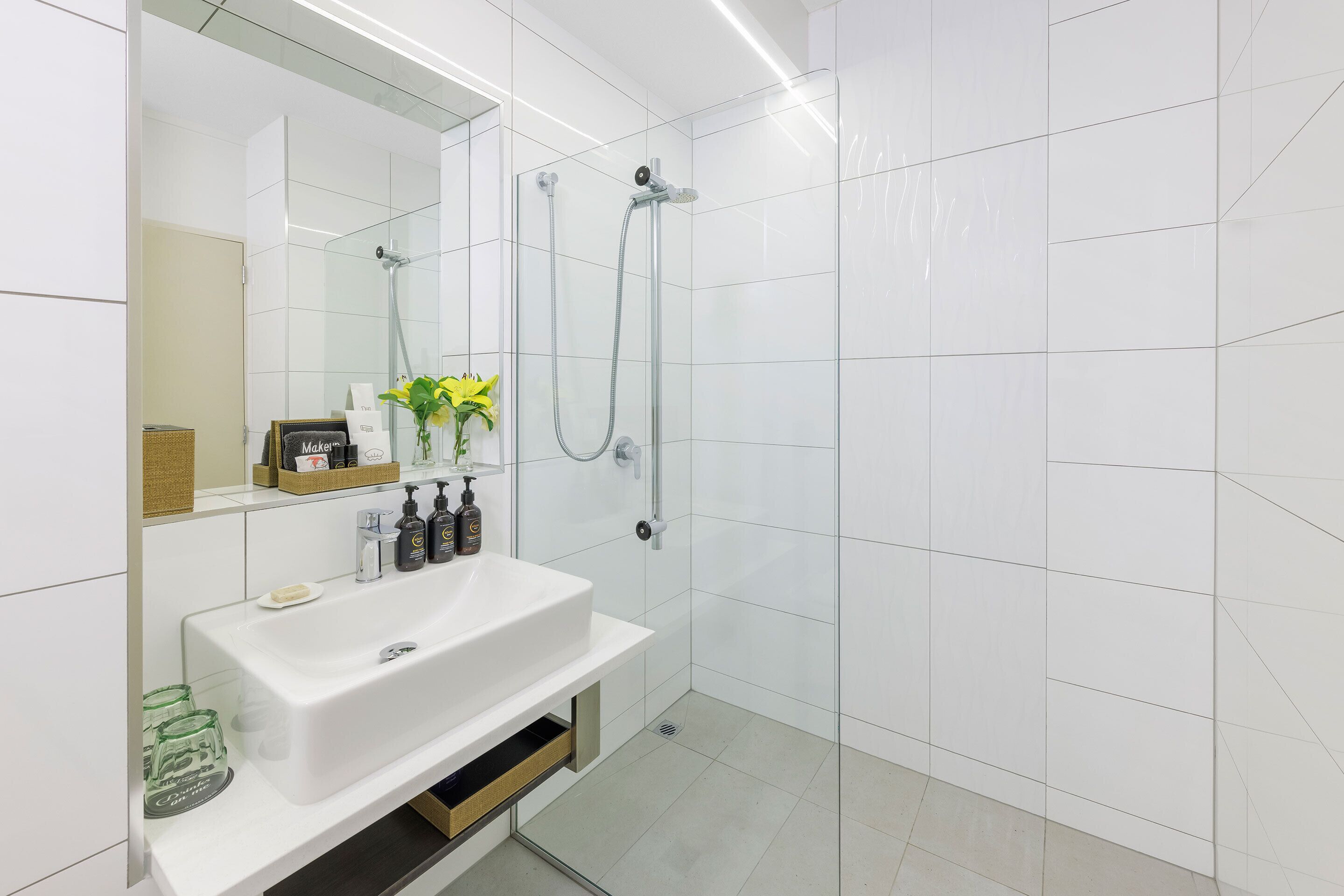 Un baño moderno con lavamanos, espejo y ducha blancos.