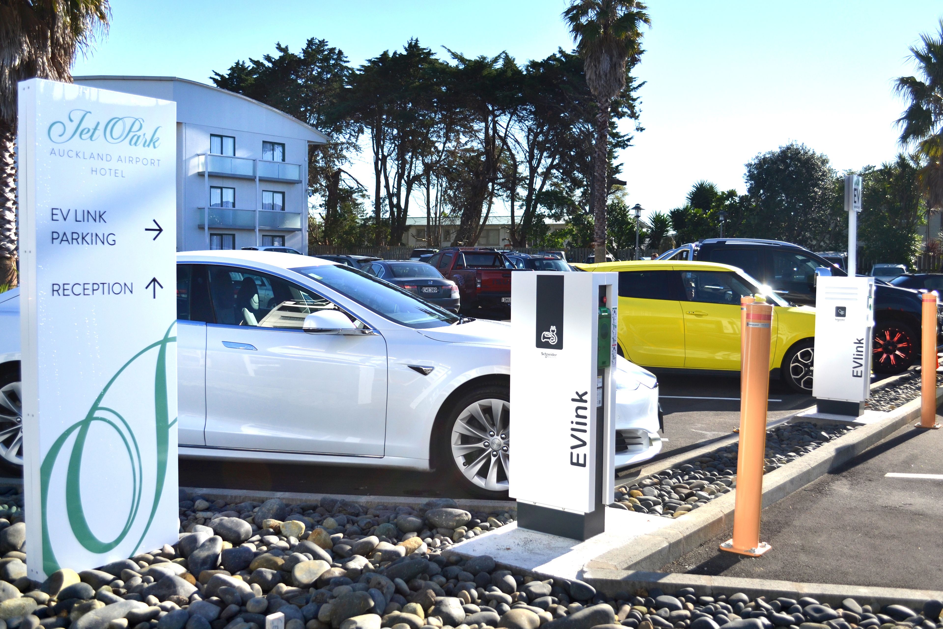 An EVLink charging station at Auckland Park Hotel, with a white car and a yellow car parked nearby.