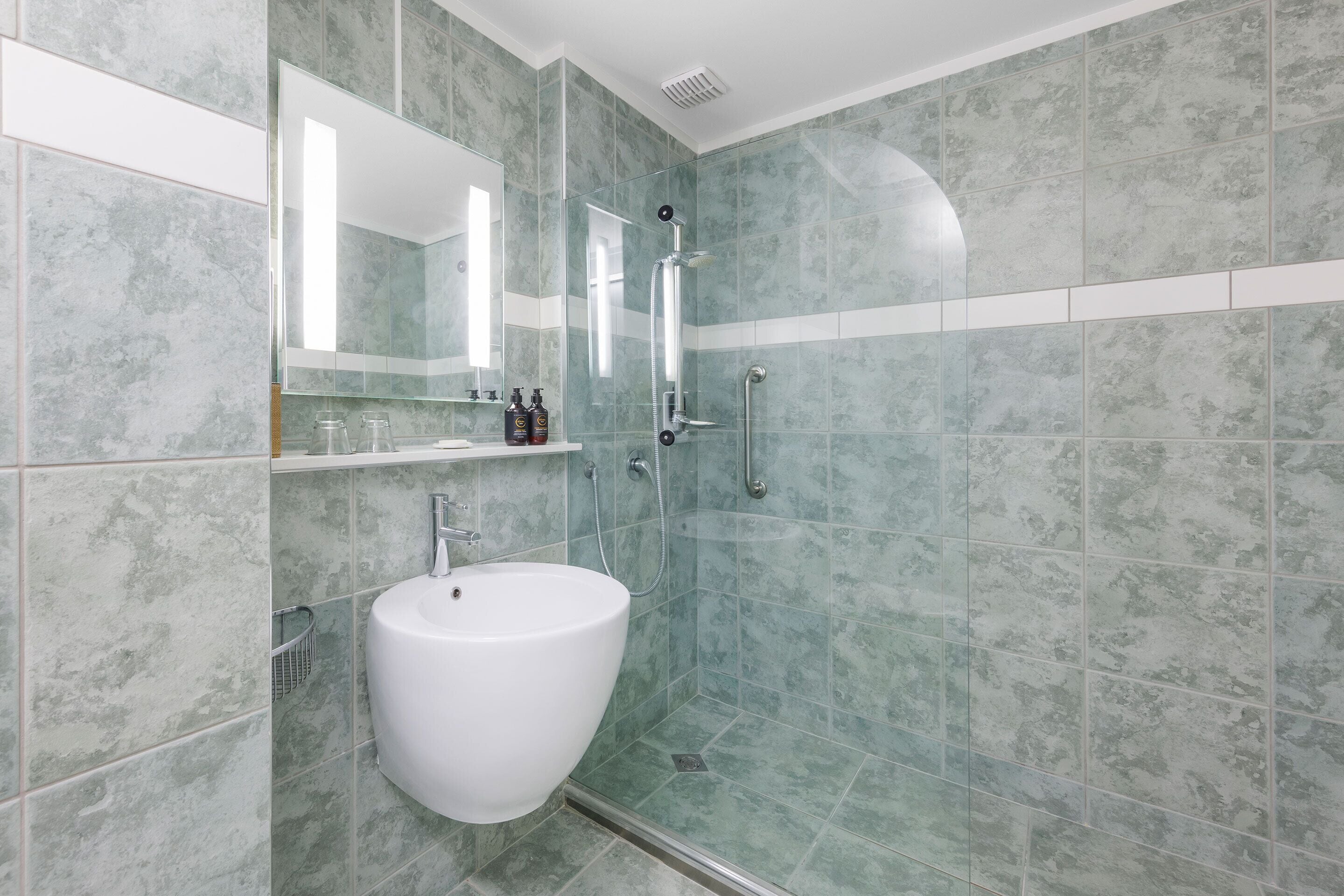 Un baño moderno con ducha envuelta en vidrio, un lavabo blanco y un espejo encima.