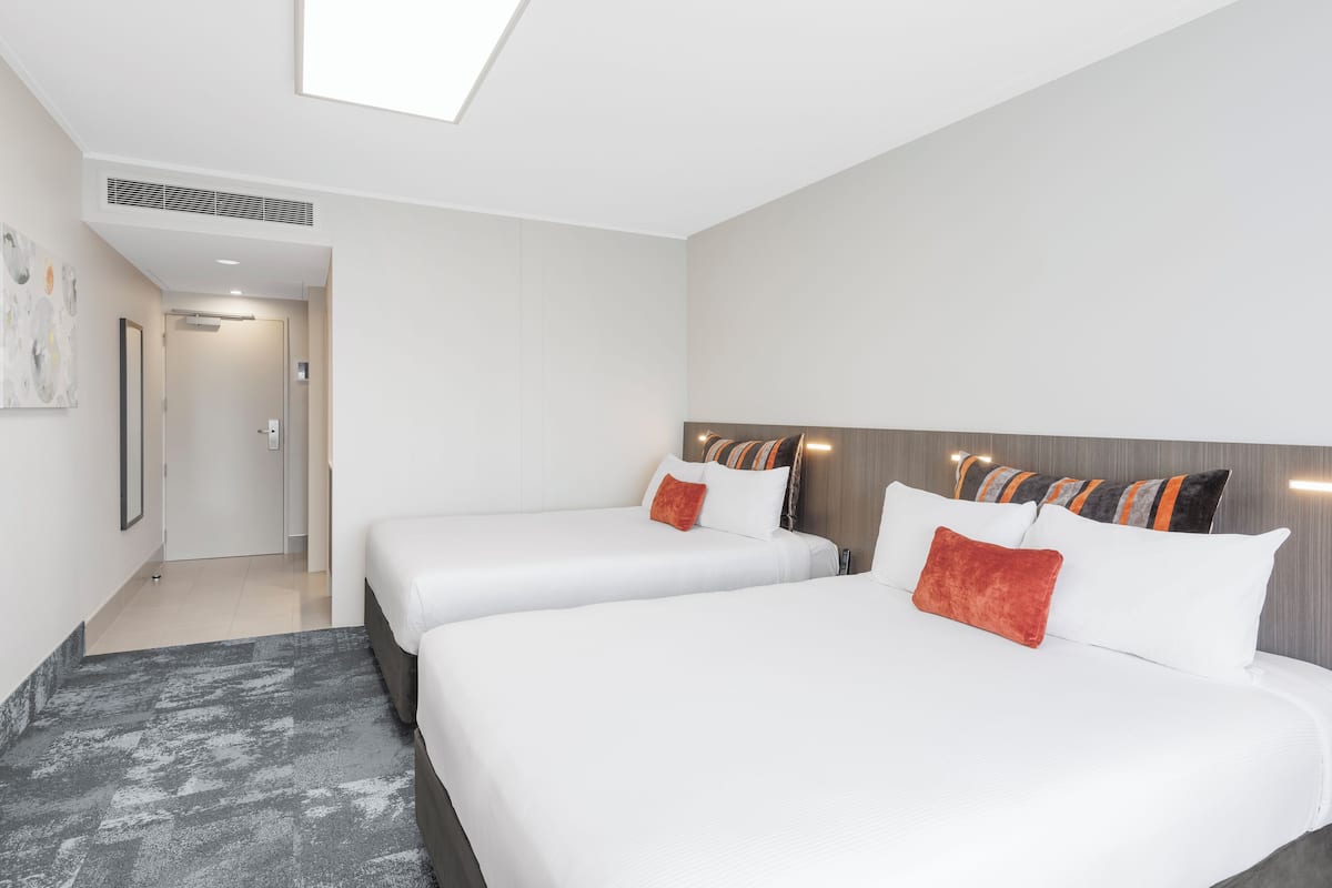 A hotel room with two beds, a large window, and a hallway leading to a bathroom.