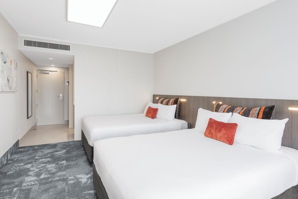Habitación de hotel con dos camas, un ventanal grande y un pasillo que conduce a un baño.