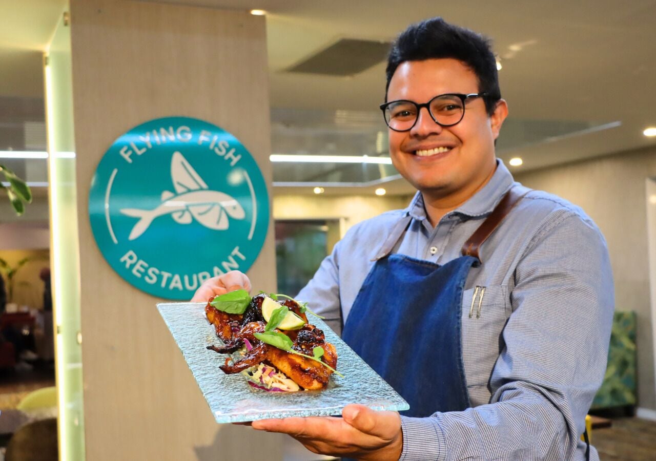 Una persona sosteniendo un plato con un logotipo que dice "FLYING FISH RESTAURANT" al fondo.
