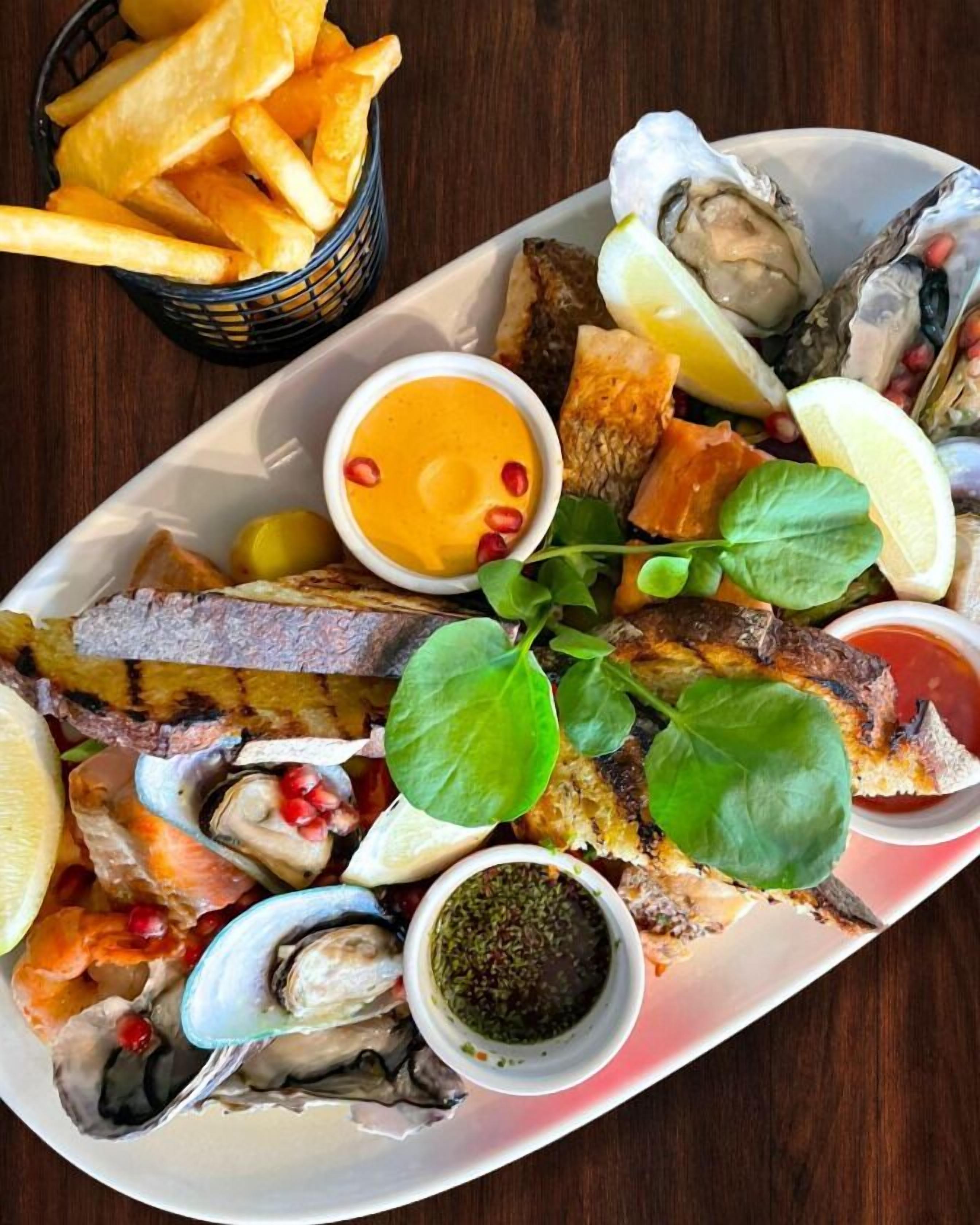 Eine Platte mit Meeresfrüchten, gegrilltem Fisch, Austern, Zitronenscheiben und Pommes Frites.