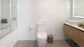 A modern bathroom with a toilet, a trash bin, a shower, and a vanity with a mirror.