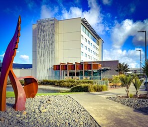 Un hotel moderno con fachada de vidrio, una piscina en la azotea y una escultura metálica distintiva.