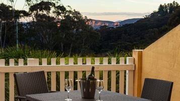 A table with two chairs and a wine bucket on a balcony with a view of trees and hills.