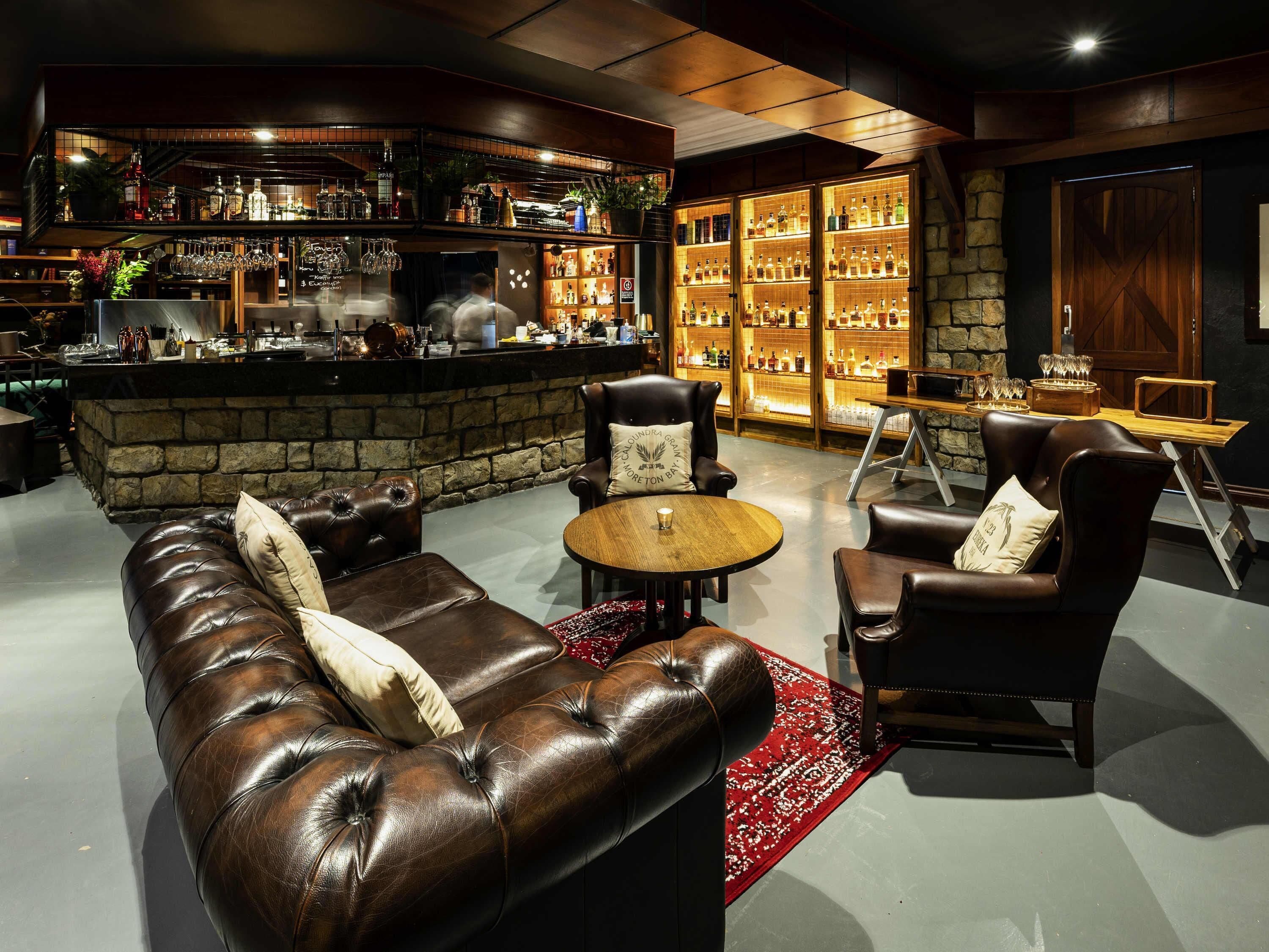 A bar area with leather seating, a stone wall, and shelves of liquor bottles.