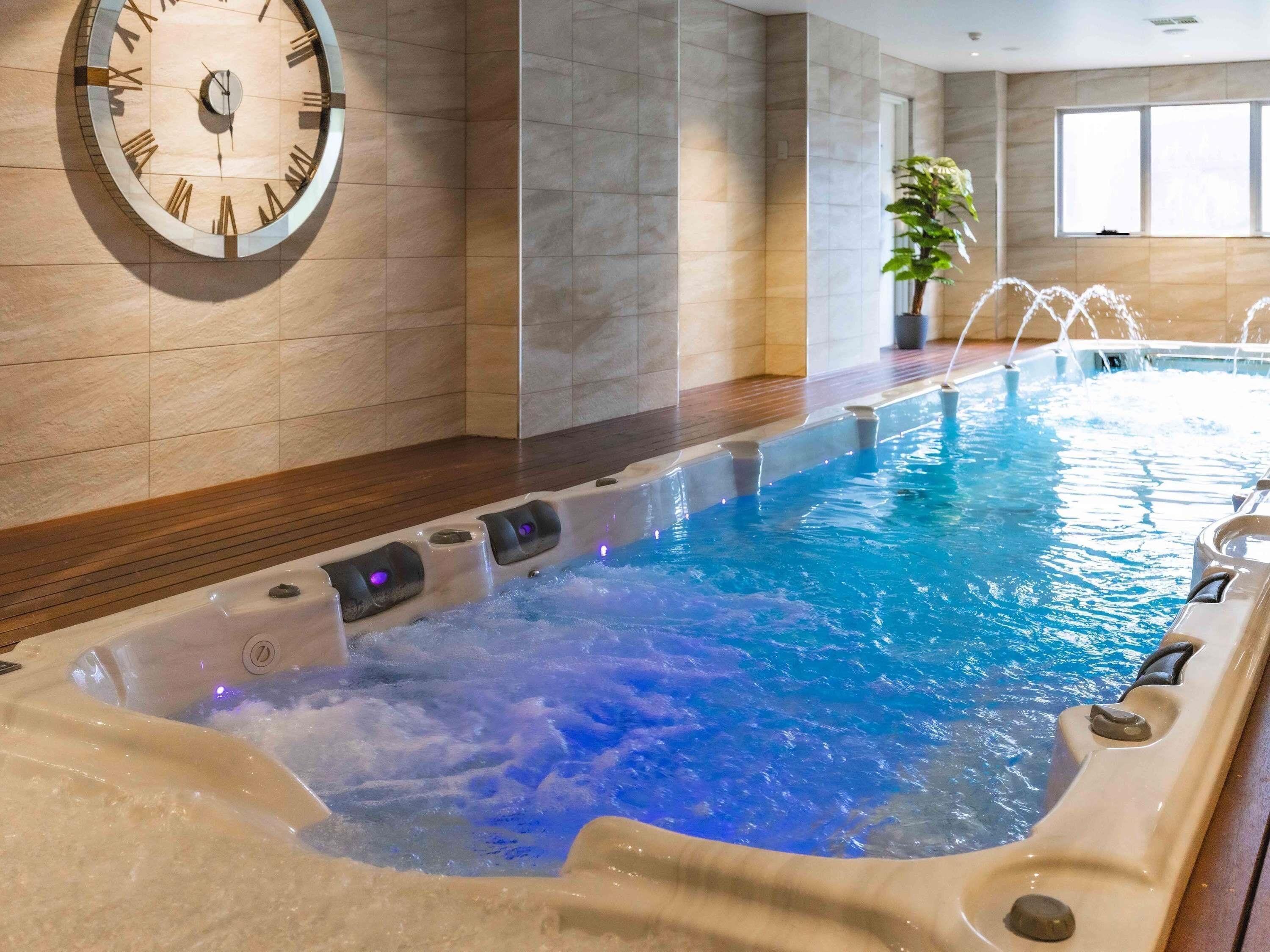 Un jacuzzi con chorros, un reloj y una planta en un ambiente interior moderno.