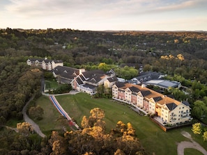 A large, multi-story building with a central courtyard, surrounded by trees and a hilly landscape.