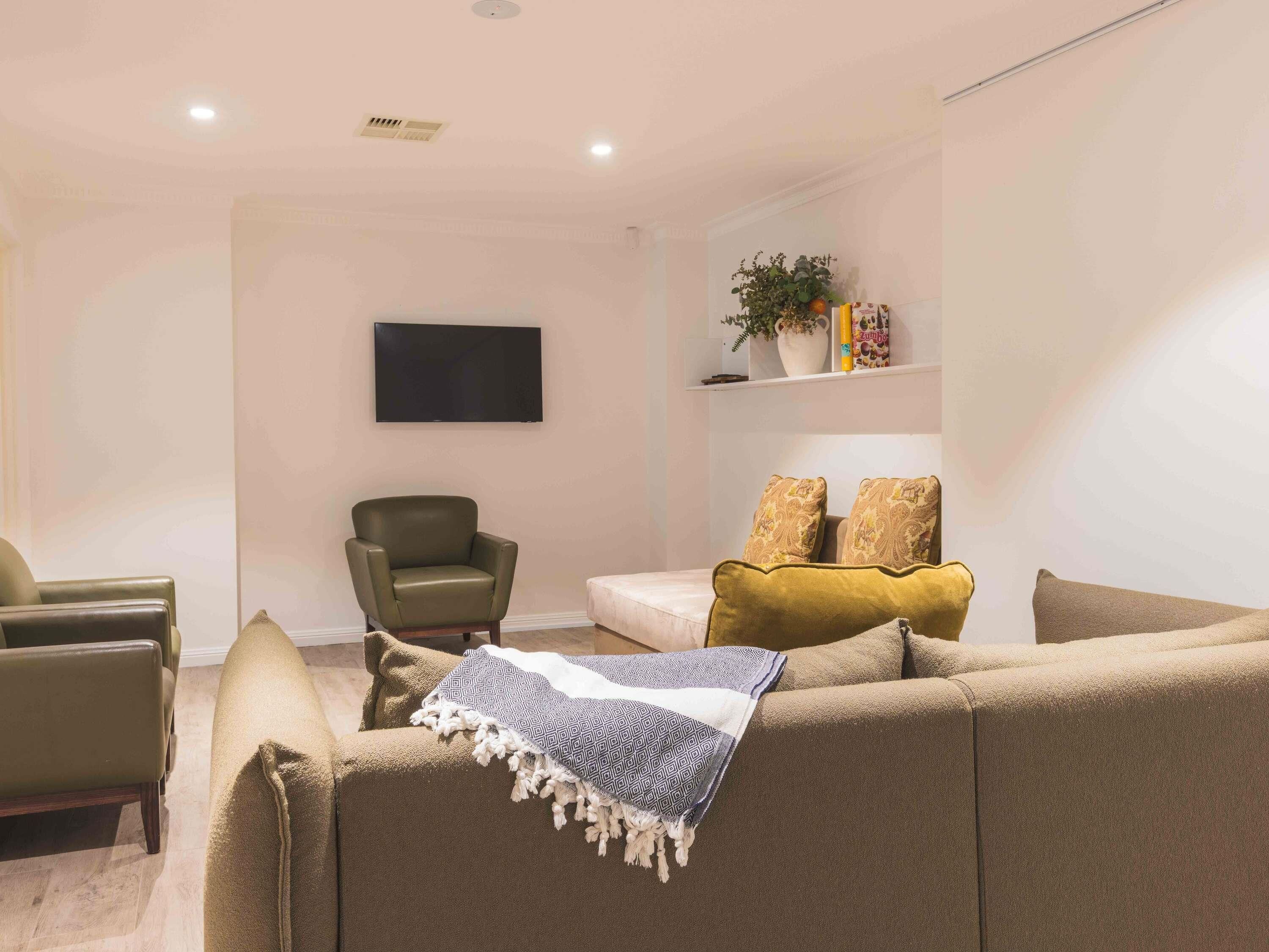 Een woonkamer met een bank, fauteuils, een televisie en een plank met decoratieve objecten.