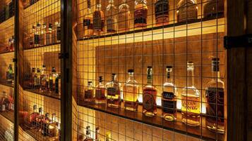 Zona de bar con estantes llenos de botellas de licores variados, incluyendo whiskey y otras bebidas espirituosas.