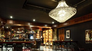 A bar with wooden furniture, a chandelier, and shelves with bottles.