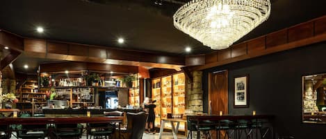 A bar with wooden furniture, a chandelier, and shelves with bottles.
