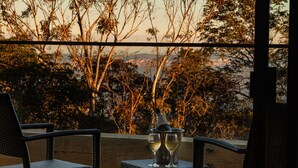 A balcony with wicker chairs and a table, two glasses of white wine, and a metal container.