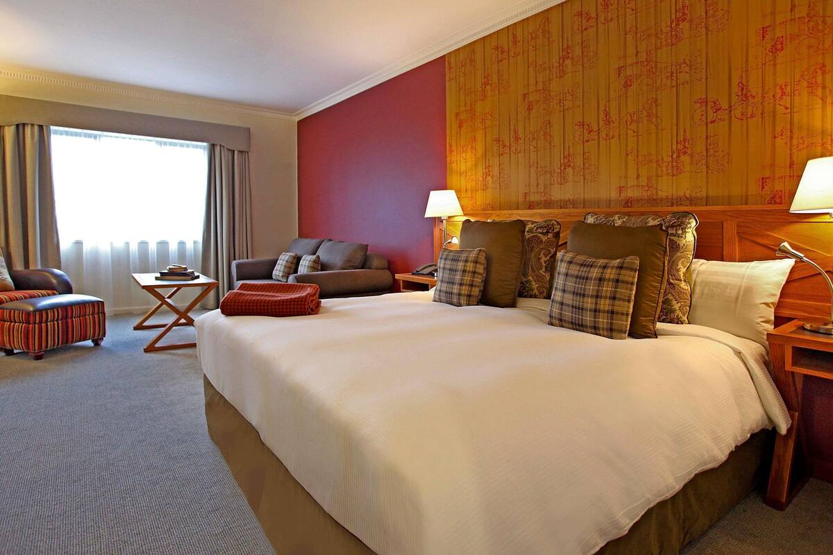 A hotel room with a large bed, a sofa, a small table, and a chair.