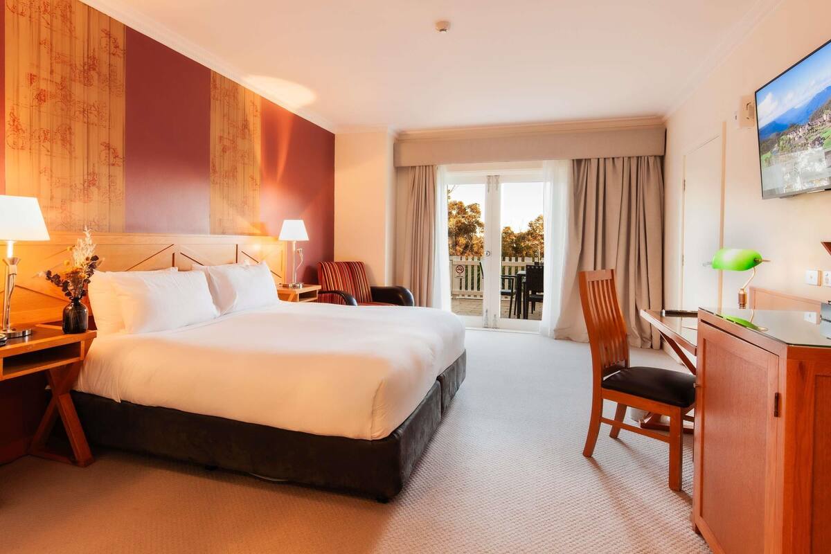 A hotel room with a bed, a desk, a chair, a TV, and a balcony with a view.