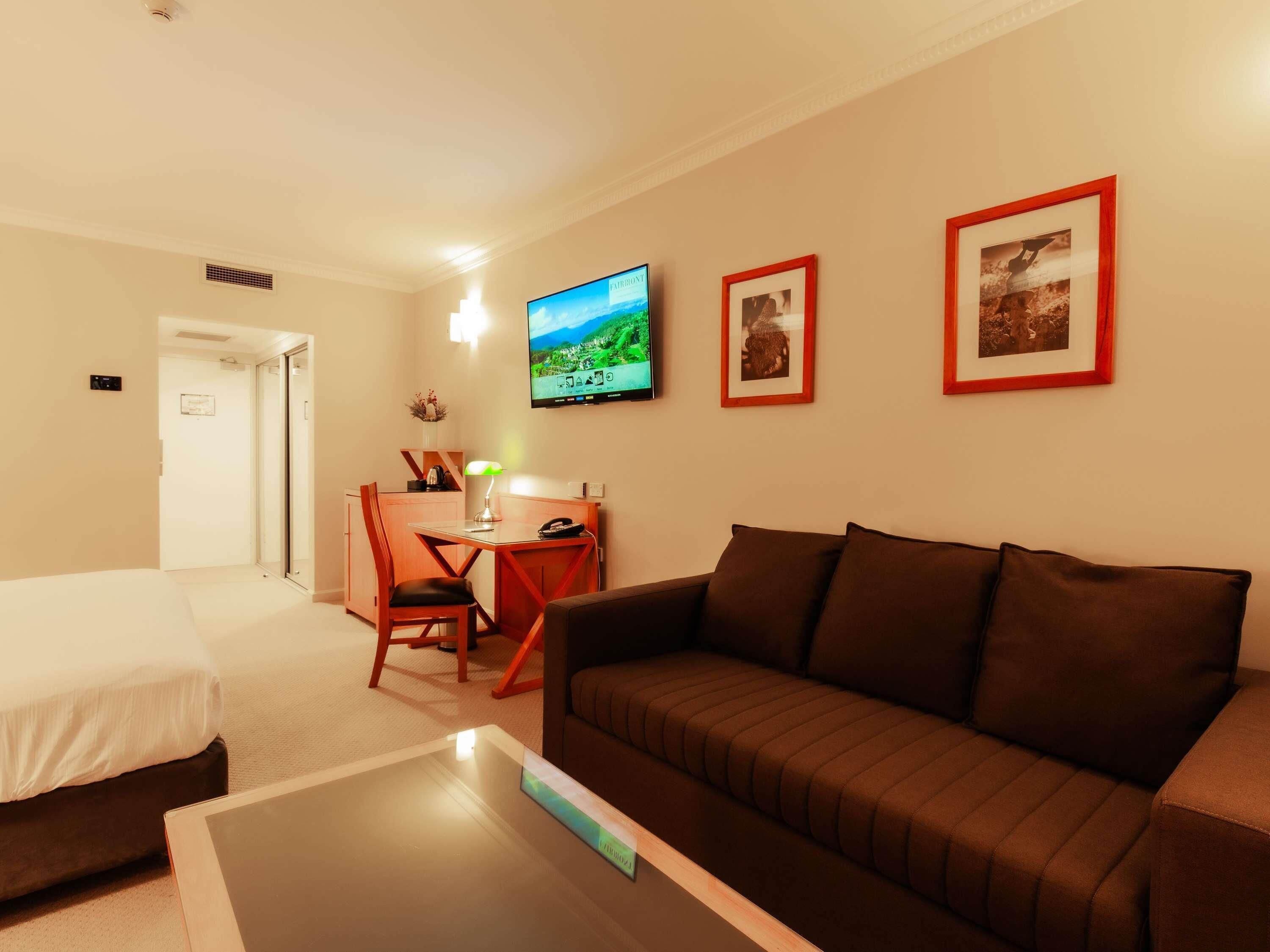Habitación de hotel con cama, sofá, escritorio con silla, televisión y cuadros en la pared.