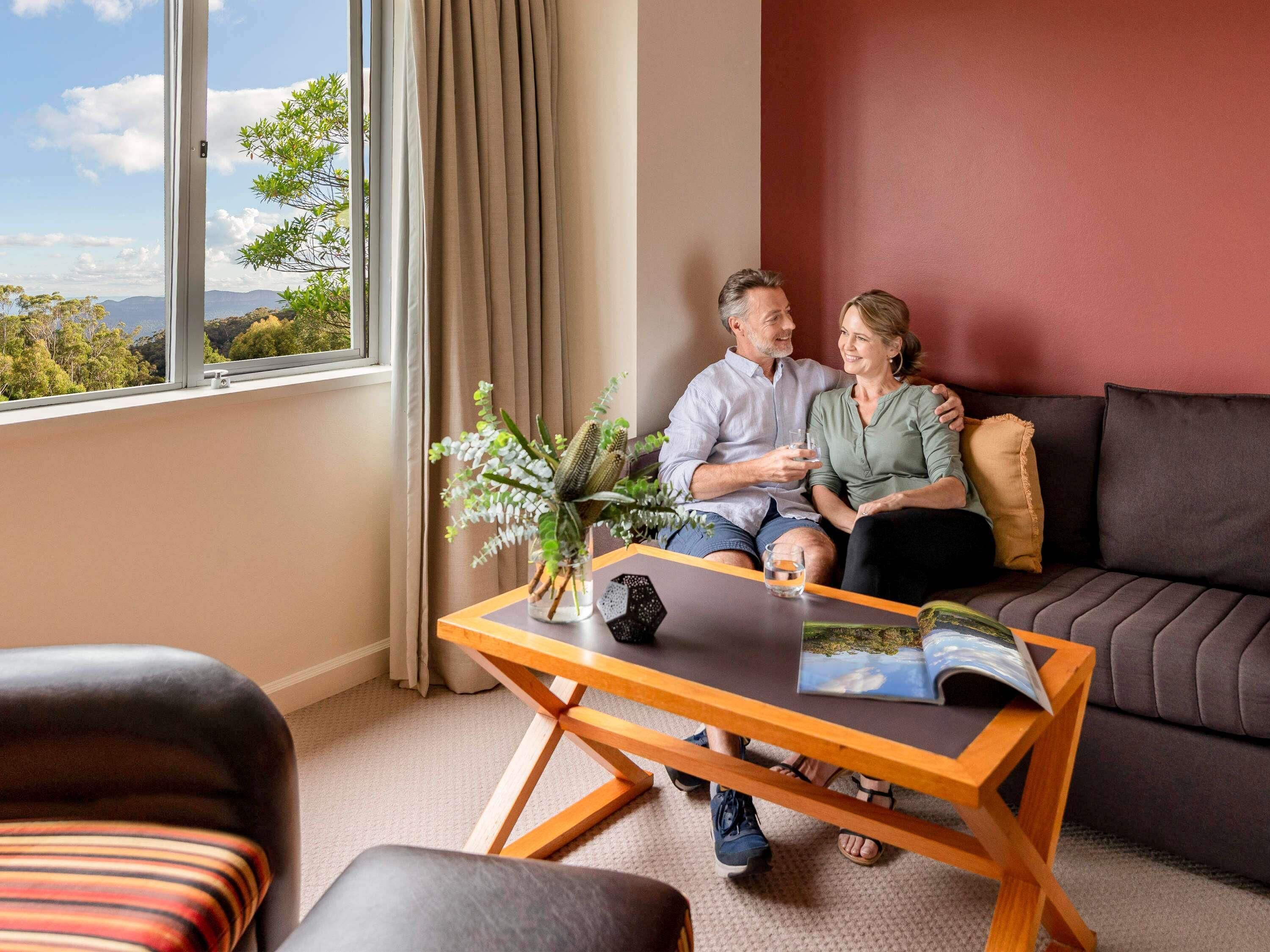 Een kamer met een groot raam, een bank, een salontafel en uitzicht op de omgeving.