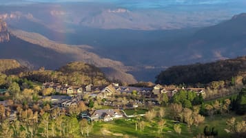 Residential homes blend seamlessly into the lush valley landscape, surrounded by well-maintained lawns and majestic mountains.