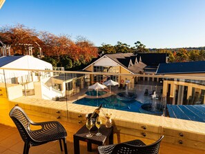A pool area with a glass balustrade, lounge chairs, and a table with a bottle and glasses. - Fairmont Resort Blue Mountains MGallery Collection (Leura)
