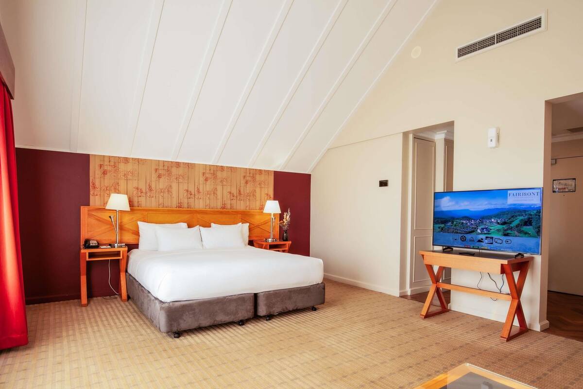 A hotel room with a bed, a TV, a wooden headboard, and a red curtain.