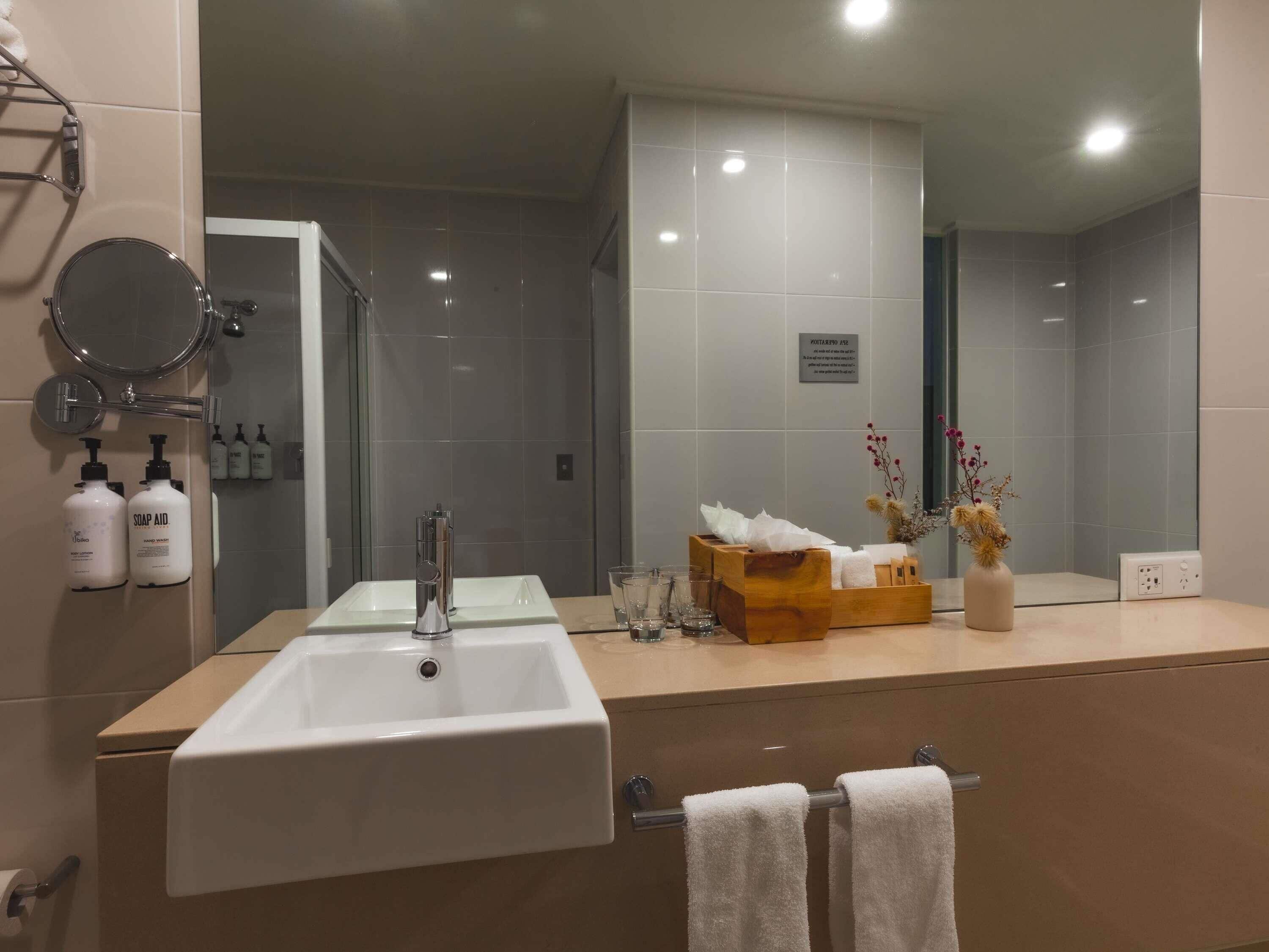 A modern bathroom with a large mirror, a white sink, and a vanity area.