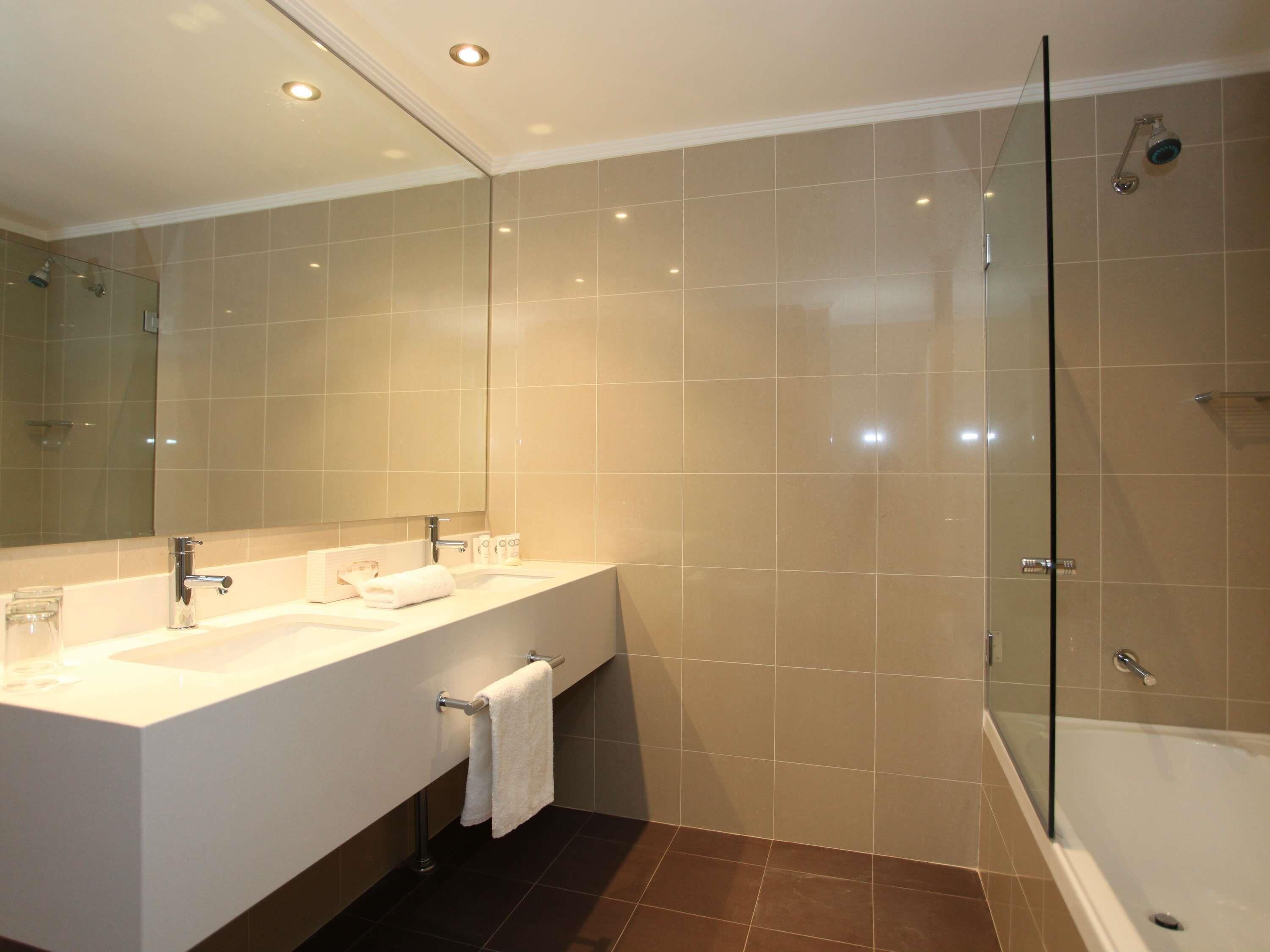 A modern bathroom with a large mirror, two sinks, a glass shower enclosure, and a bathtub.