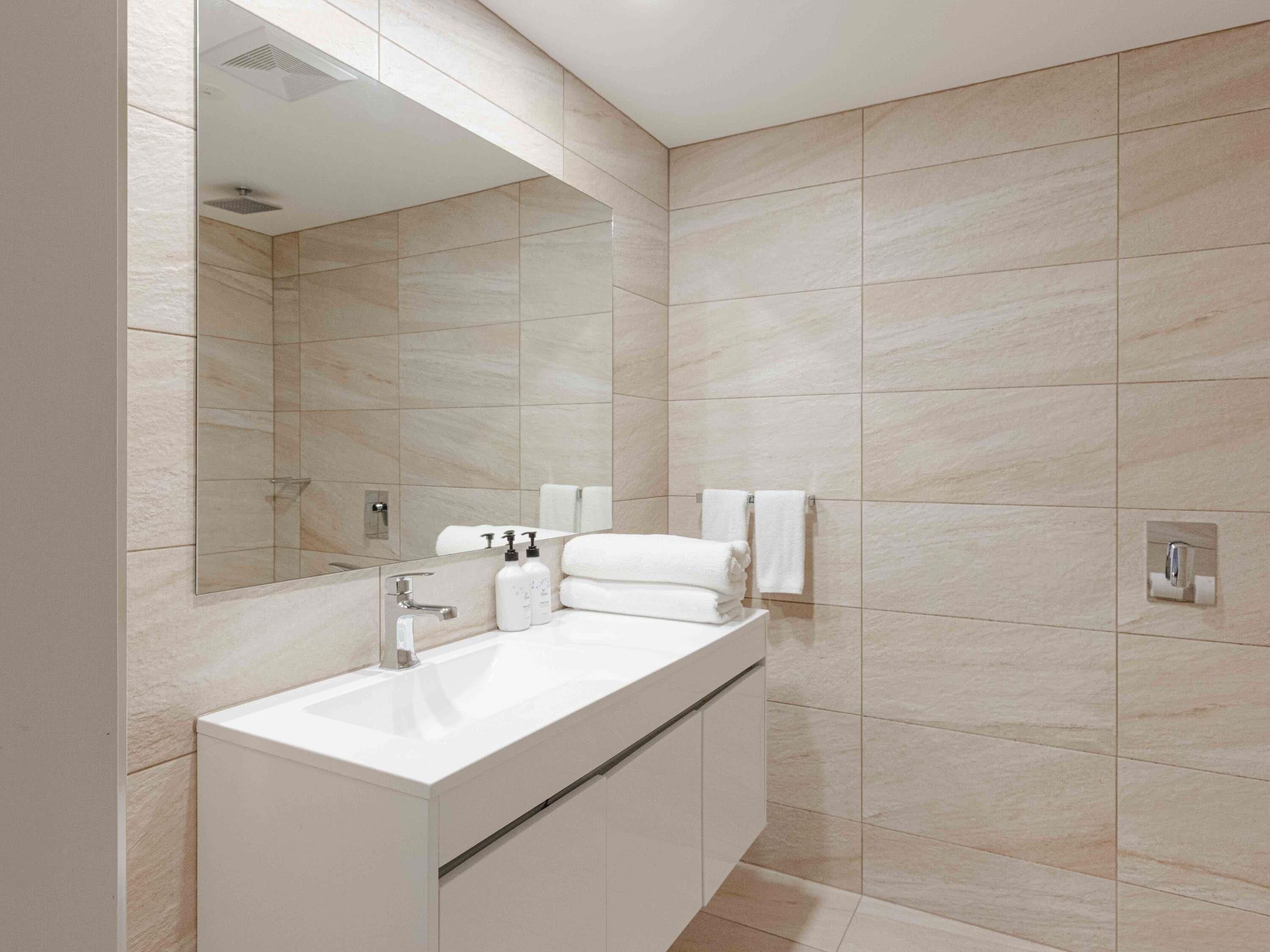 A modern bathroom with a large mirror, a white sink, and a shower area.