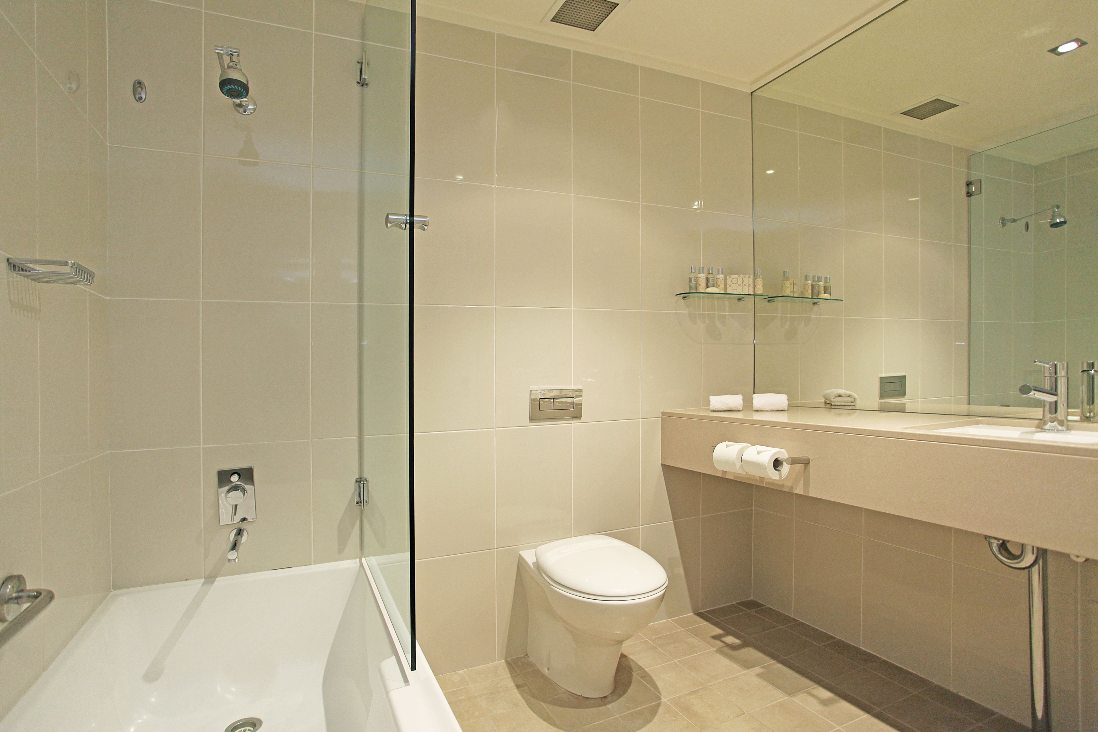 A modern bathroom with a glass-enclosed shower, a white bathtub, and a toilet.