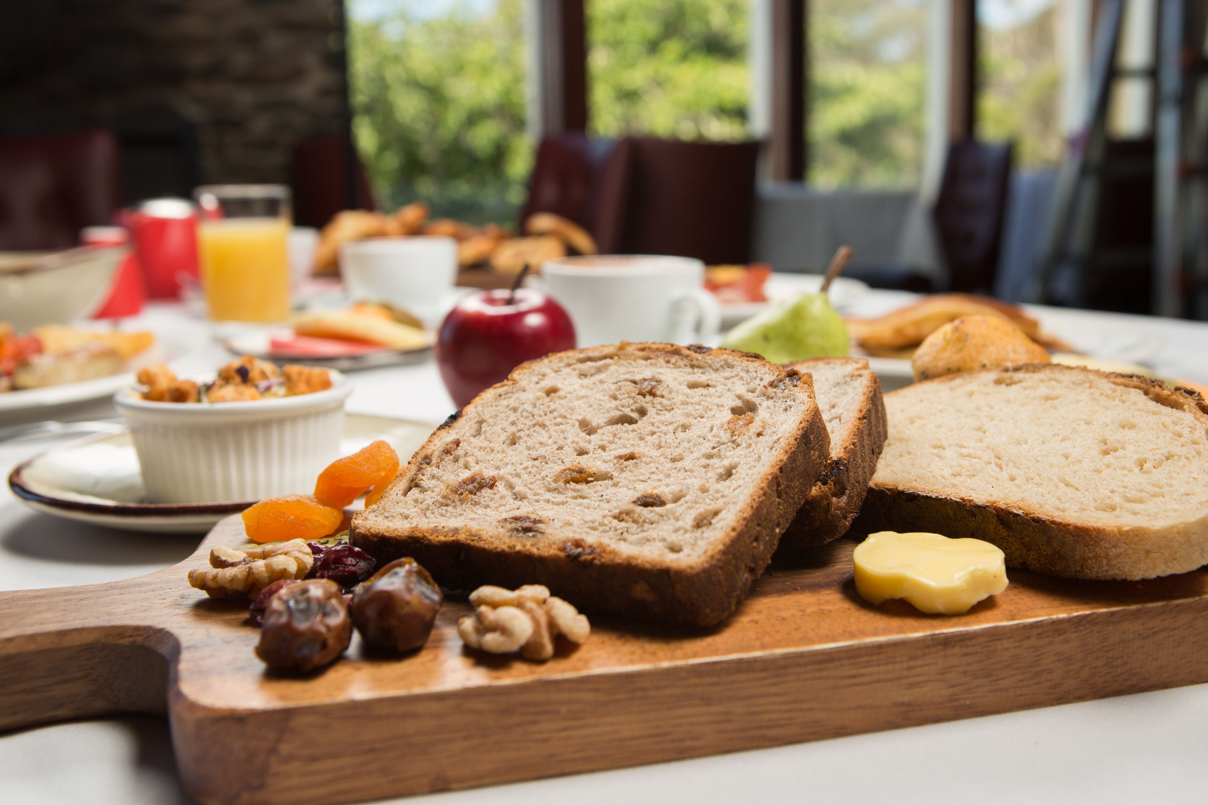 Une table de petit-déjeuner avec du pain, du beurre, des fruits et un verre de jus d’orange.
