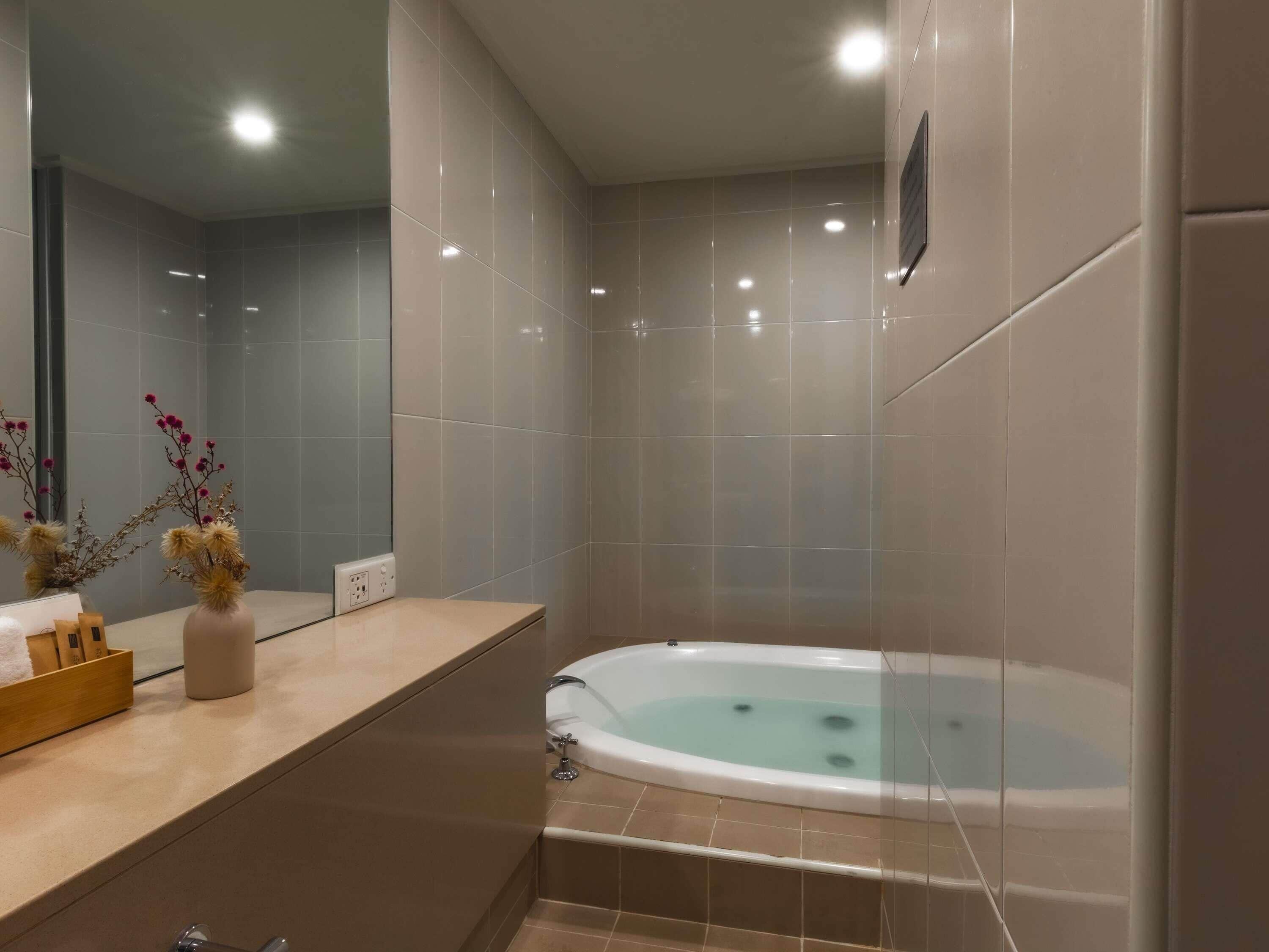 Un baño moderno con una bañera, un espejo y un florero con flores secas.