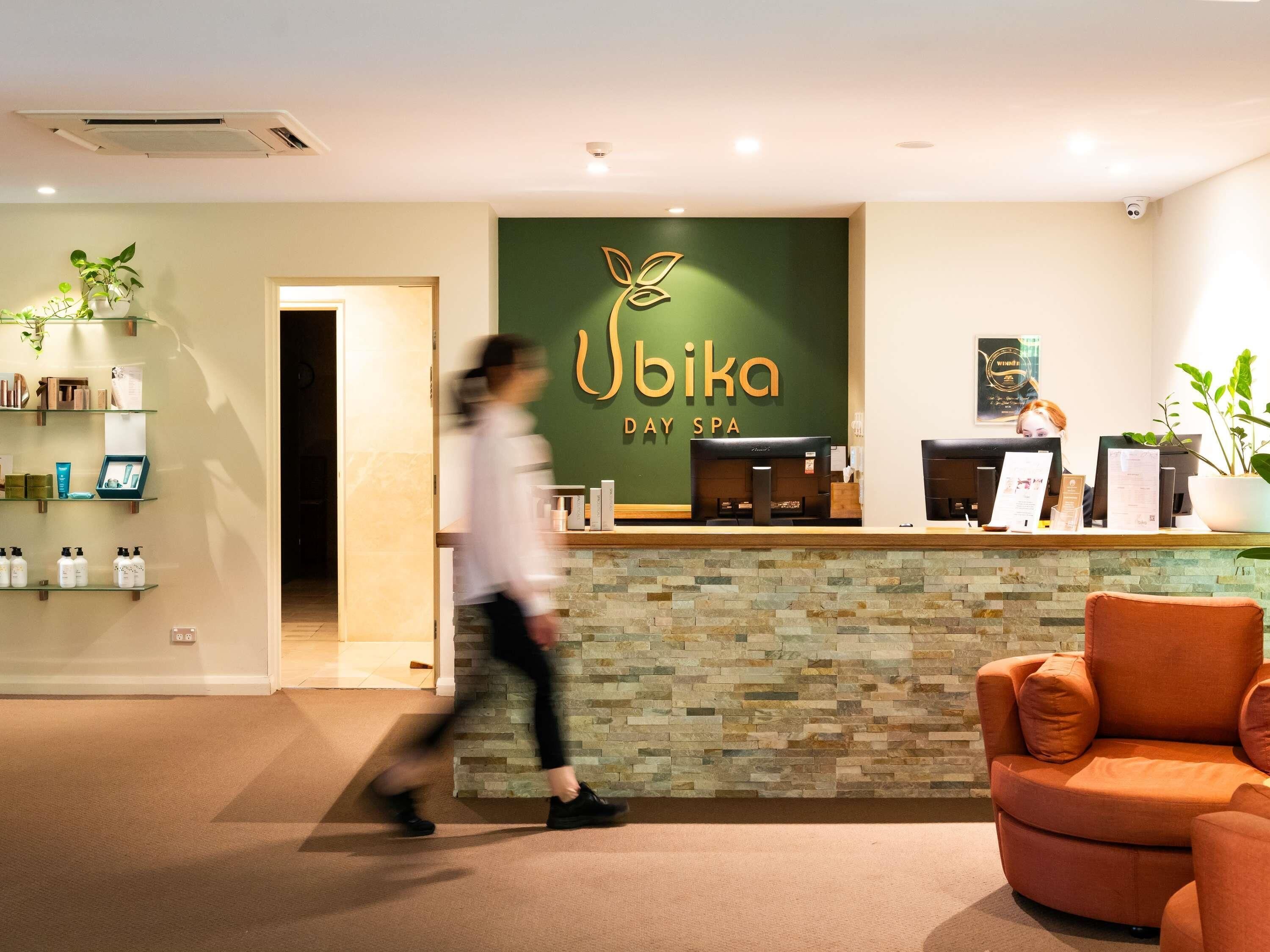 A reception area with a reception desk, a wall-mounted sign reading 'Ubika Day Spa,' and a potted plant to the left.