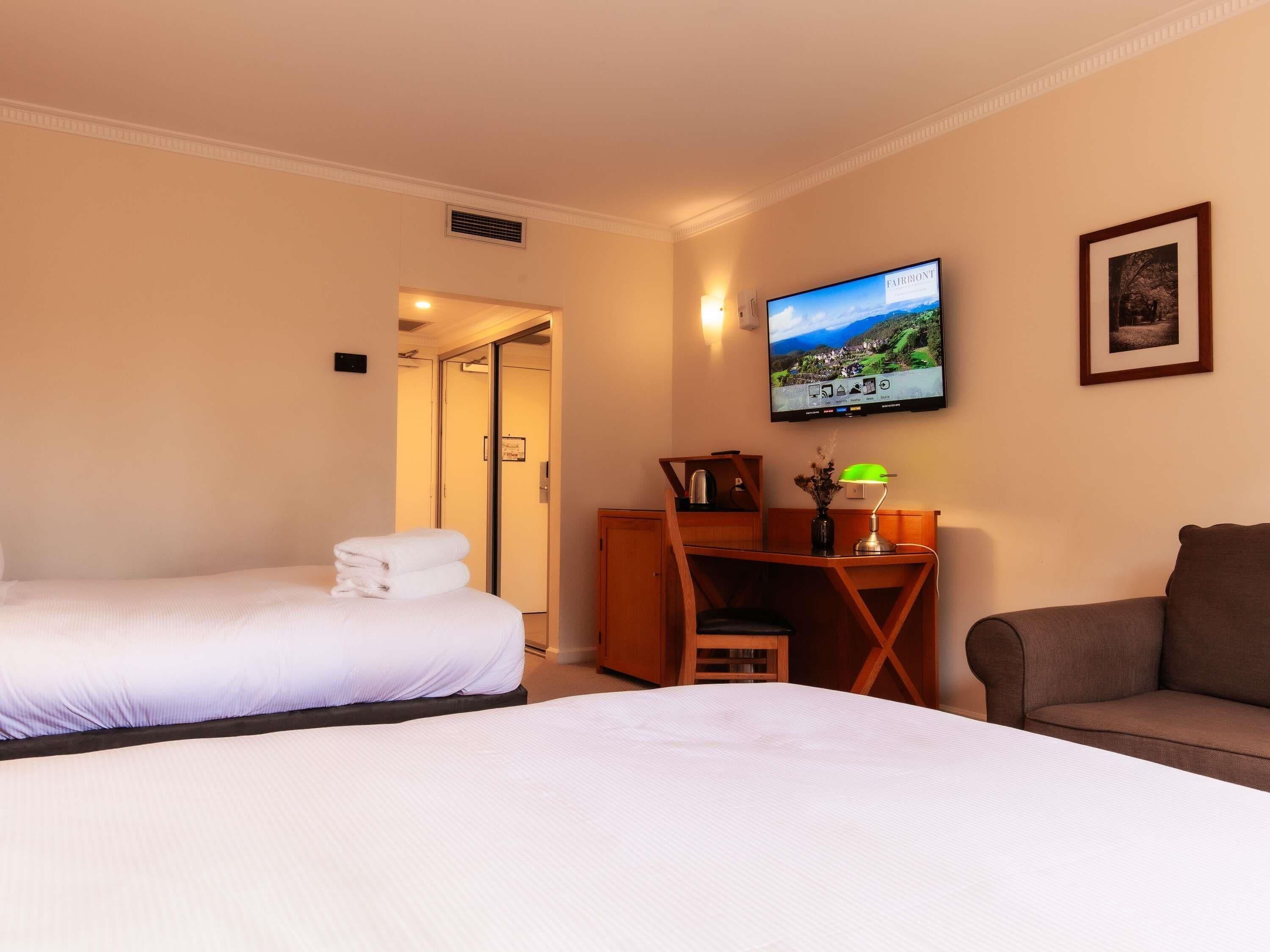 A hotel room with two beds, a desk with a lamp, a TV, and a framed picture on the wall.
