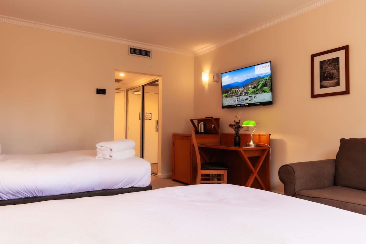 A hotel room with two beds, a desk with a lamp, a TV, and a framed picture on the wall.