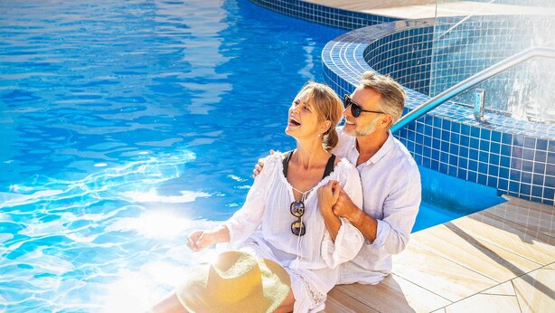 A couple sitting by a swimming pool with tiled edges and a sunlit deck.