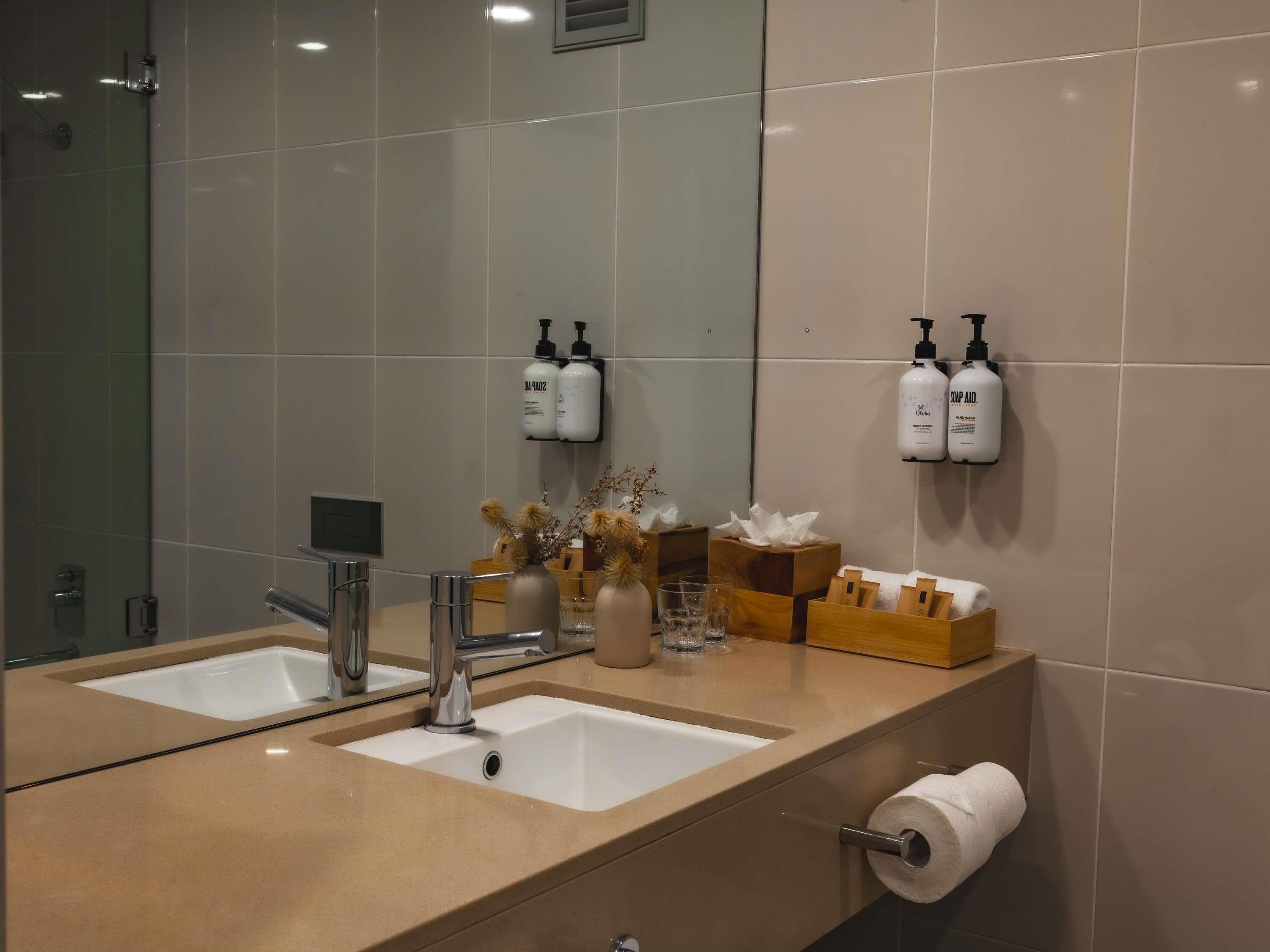 A modern bathroom with two sinks, a mirror, and toiletries on the wall.