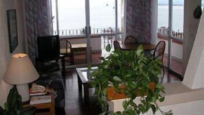 A living room with a TV, a ceiling fan, a dining table, and a large window overlooking the sea. - Hotel Suites La Siesta (Puerto Vallarta)