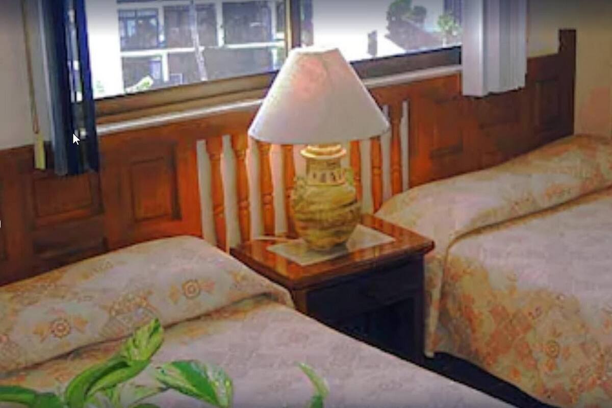 Een hotelkamer met twee bedden, een nachtkastje met een lamp en een raam met gordijnen.