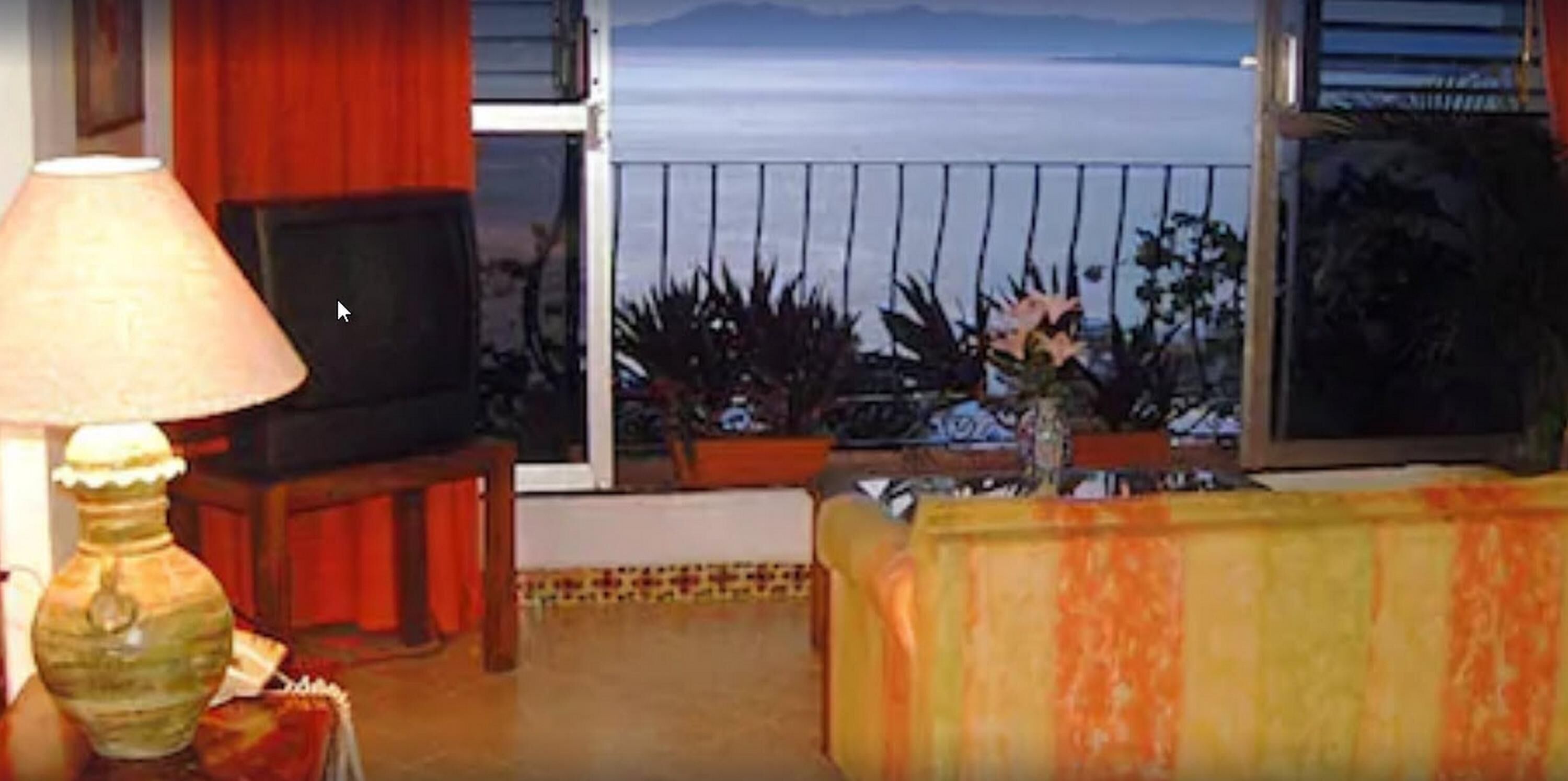 A living room with a TV, a lamp, and a view of the ocean.