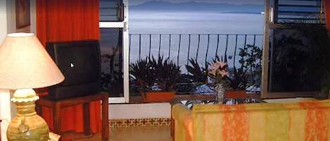 A living room with a TV, a lamp, and a view of the ocean.