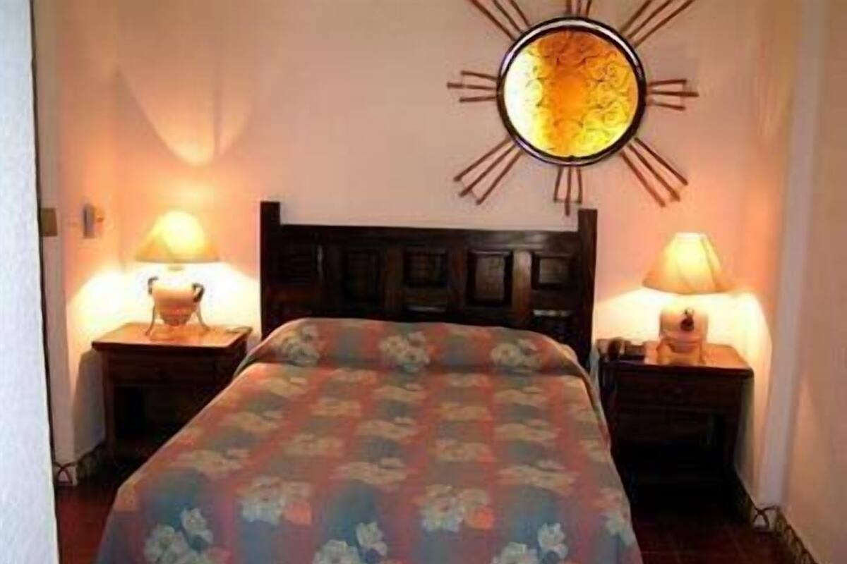 Een hotelkamer met een bed, twee nachtkastjes met lampen en een wandklok.