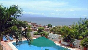A pool area with a view of the sea, surrounded by greenery and a few lounge chairs. - Hotel Suites La Siesta (Puerto Vallarta)
