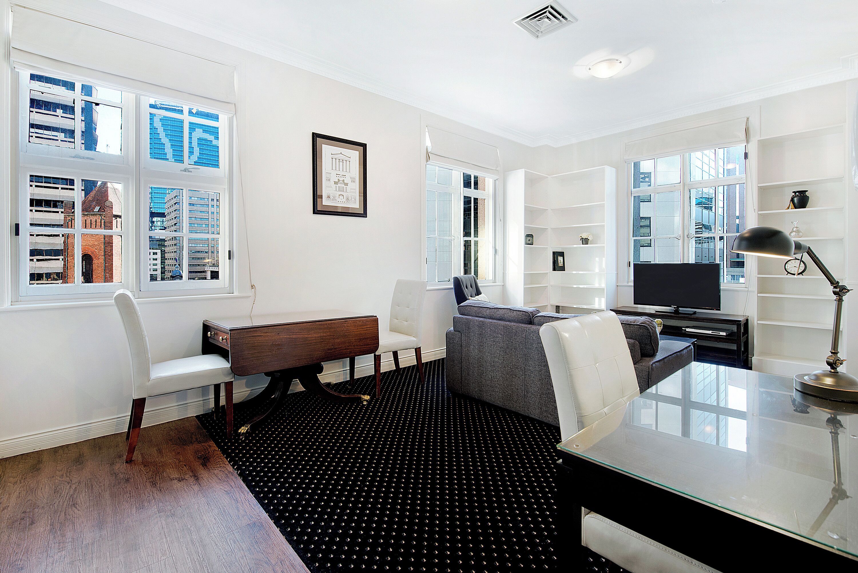 A modern living room with a glass coffee table, a sofa, a white chair, a desk, and a television.